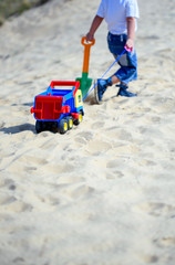 Boy on the beach with a toy car in the sand