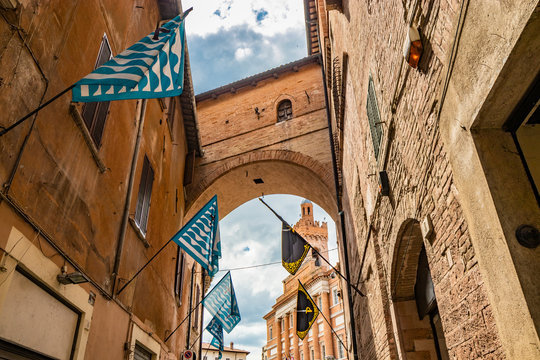An alley in the historic center of Foligno, with blue, black and yellow flags of the districts. At the bottom, under the arch, you can see the Town Hall of the city. Perugia, Umbria, Italy.