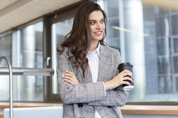 Attractive smiling businesswoman standing in the office with a cup of coffee.