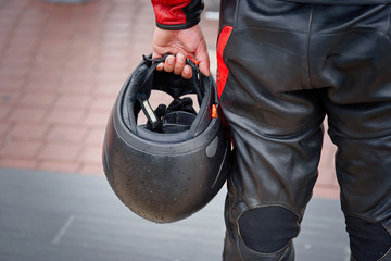Biker in leather panths hold in hand black motorcycle helmet. Armor and special protective moto...