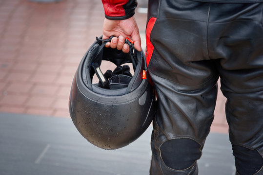 Biker In Leather Panths Hold In Hand Black Motorcycle Helmet. Armor And Special Protective Moto Equipment For Bikers And Moto Riders