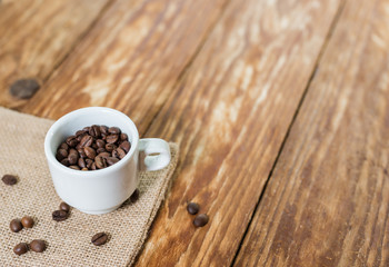 Delicious brown coffee beans in an Italian espresso cup on a wood table..
