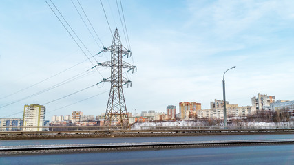 In the foreground is a clean two-lane road. On it is a close-up view of a high-voltage transmission line pylon. Next - a residential neighborhood.