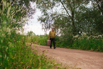 An elderly man travels with a suitcase. A sad and tired villager is on the road to a long way.