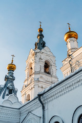 we see the bell tower of Holy Trinity Monastery of Stefanov. It is illuminated by the rays of the setting sun. On the right and on the left, other buildings of the monastery are visible.
