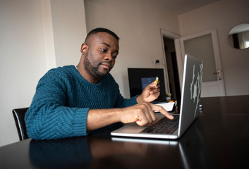 Black man makes purchases online using the card in the online store. Pays for utilities online. Buying goods with credit ore debit card. Man ordering a lunch from the house