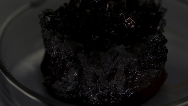 Beautiful unusual gray-black crystal stone cassiterite with a metallic sheen standing in the glass stand. Stock footage. Close up for shining crystal standing on the table.