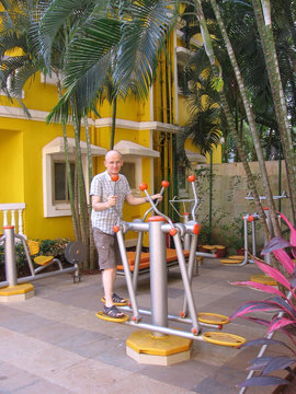 A middle aged man with glasses is engaged on street gym. Yellow wall, palm trees. Vertical photo