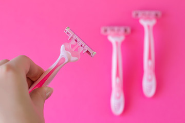 Pink razor in a female hand on a pink minimalistic background. Razor for personal hygiene for hair removal