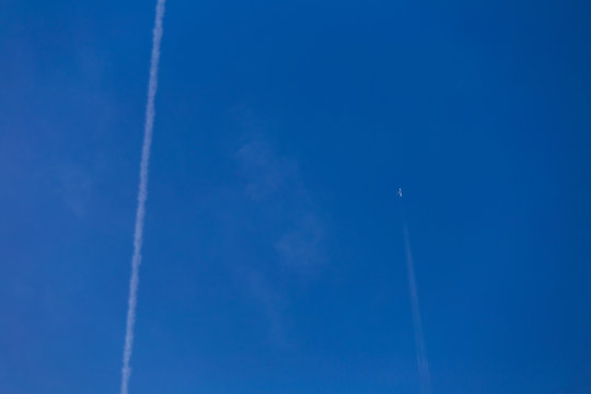Airplane flying in blue sky. White trails from planes as seen from earth. Horizontal color photography.
