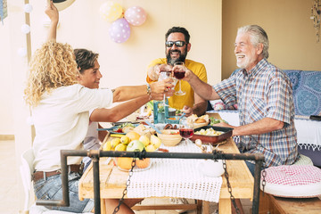 Family toasting with big smiles. enjoying bbq outdoors in the terrace. Wooden table.  Bright light and balloons on background. Focus on man with black hair