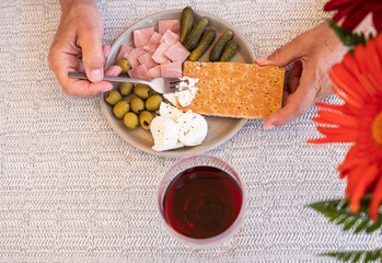 Above view of small dish full of snack like dried bread, jam, light cheese,olives and cucumber. Dieting with a red wine glass. Flowers on the right side