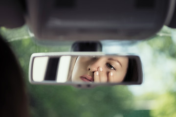 Reflection of a beautiful young woman face in the car rear view mirror. concept