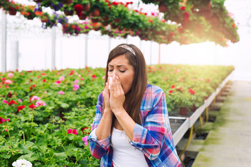 Beautiful young woman with allergy symptoms blowing nose in white tissue due to pollen in the air. Allergy problems.