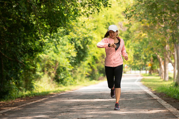 Asia woman runner running while checking heart rate  at park, female in sport cloth jogging while looking on watch at park, healthy sport active lifestyle concept