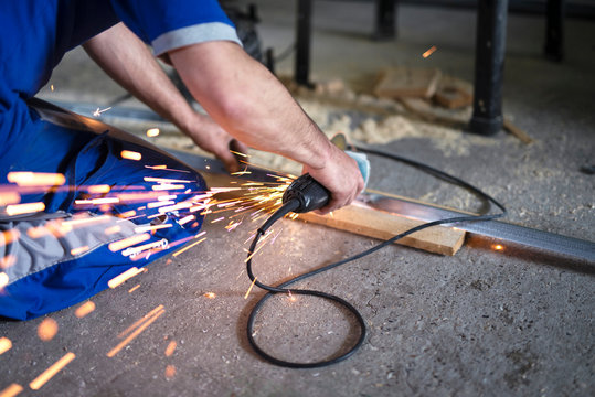 Close up view of manual worker using ginder to cut steel in metal workshop. Sparks flying around.