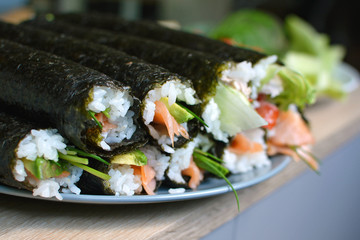 Whole homemade sushi rolls with white rice, salmon and salad in nori seaweed sheets before cutting piled up on a plate