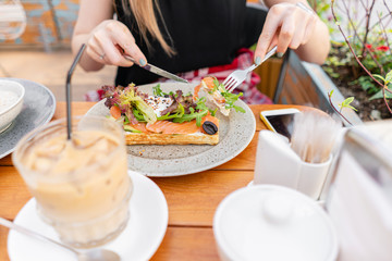Traditional Belgian waffle with salmon, lettuce leaves and poached egg. A young woman is having Breakfast in a summer cafe, hands with a fork and a knife close-up. Cold coffee with ice cubes
