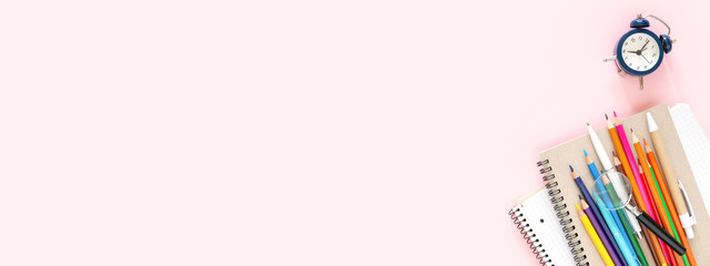 School stationary on pink background. Notebooks, pens, color pencils and alarm clock. Back to...