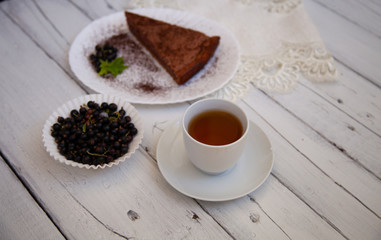 chocolate cake slice with a white cup of tea and a handful of currants