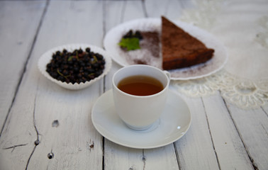 chocolate cake slice with a white cup of tea and a handful of currants