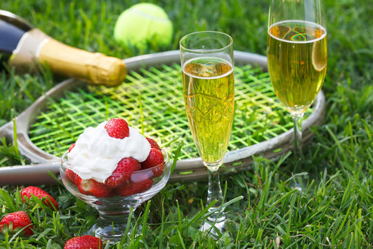 Strawberries with whipped cream, glasses with champagne and tennis equipment on Wimbledon tournament grass. Wimbledon Grand slam celebration concept.