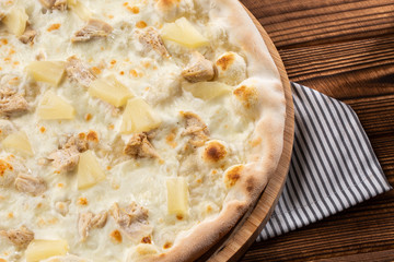 Pizza topped with sauce, chicken, cheese and pineapple serve on wooden plate on wooden table. Photo of Hawaiian pizza. 