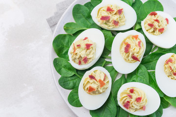 Deviled eggs stuffed with avocado, egg yolk and mayonnaise filling, garnished with bacon, on spinach leaves, horizontal, top view copy space