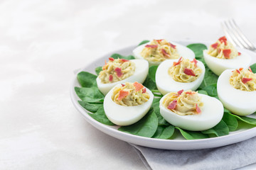 Deviled eggs stuffed with avocado, egg yolk and mayonnaise filling, garnished with bacon on spinach leaves, horizontal copy space