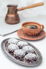 Swedish sweets chocolate balls or chokladbollar, made from oats, cocoa, butter and coconut, on  metal plate, served with coffee,  vertical