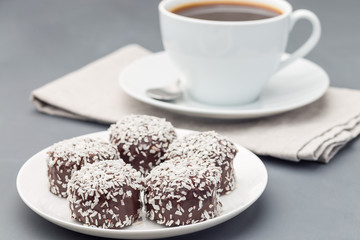 Swedish sweets chocolate balls or chokladbollar, made from oats, cocoa, butter and coconut, on white plate, served with coffee,  horizontal