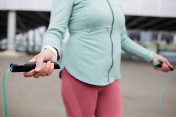 Hands of contemporary active mature female holding skipping rope while training with it outdoors in urban environment