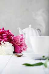 Fresh beautiful flowers peonies and a ceramic white cup with tea for breakfast
