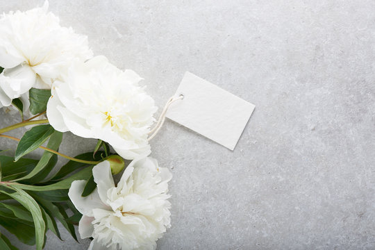 Beautiful white peony flowers and tag on gray stone background.