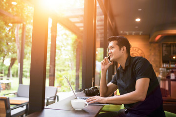 Stylish modern guy talking with a smartphone and using a laptop in a coffee shop