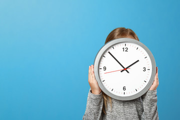 The little girl is hiding behind a big clock on a blue background. The concept of education,...