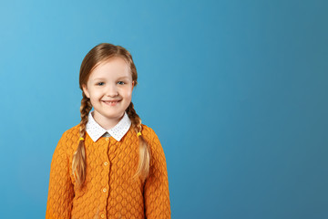 Closeup portrait of a little girl schoolgirl. Pretty child in a yellow sweater on a blue background. Copy space