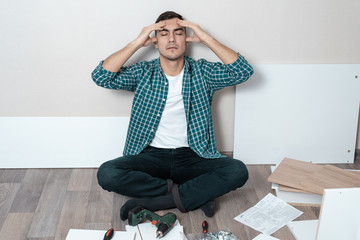 Portrait of a man on the floor holding his head, the difficulty of assembling furniture