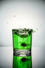 The splashes from the falling ice in green cocktail