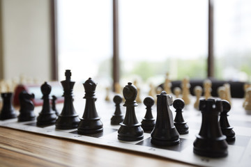 Arranged wooden chess pieces standing in perfect order on table in front of window in classroom of...