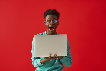 Positive Afro American guy with gadget posing in studio on red background