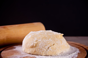 fresh raw dough for pizza or bread baking on wooden cutting board on black background