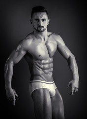 Fototapeta na wymiar Man posing and straining his muscules. Strong, muscular guy on a black background. Sport theme. Comfortable underwear. Confident look, healthy eating. Young attractive man.