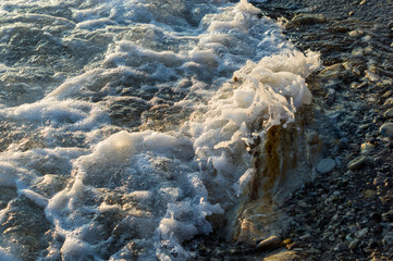 pebble stones on the sea beach, the rolling waves of the sea with foam
