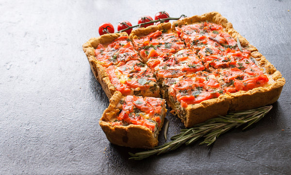 Rectangular quiche with salmon, spinach and cream on a black wooden table. French cuisine. The view from the top. Copy space.