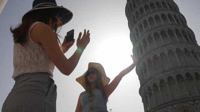 A woman takes a picture of her friend and tells her how to touch the Leaning Tower on photo. Italy - Pisa