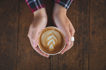 Woman hand holding a cup of coffee on an old wooden table, top view