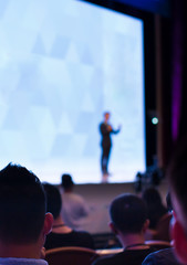 "Speaker giving a talk at a corporate business conference. Audience in hall with presenter in front of presentation screen. Corporate executive giving speech during business and entrepreneur seminar. 