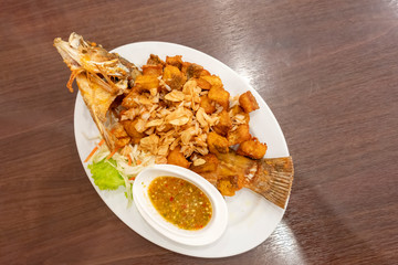 Deep Snapper Fried with fish sauce the delicious favorite menu Thai sea food on wooden table