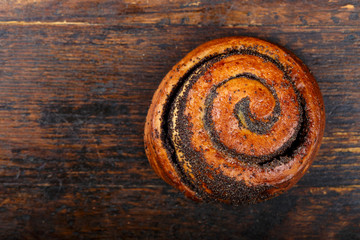 Sweet homemade bun with poppy seeds on a wooden background